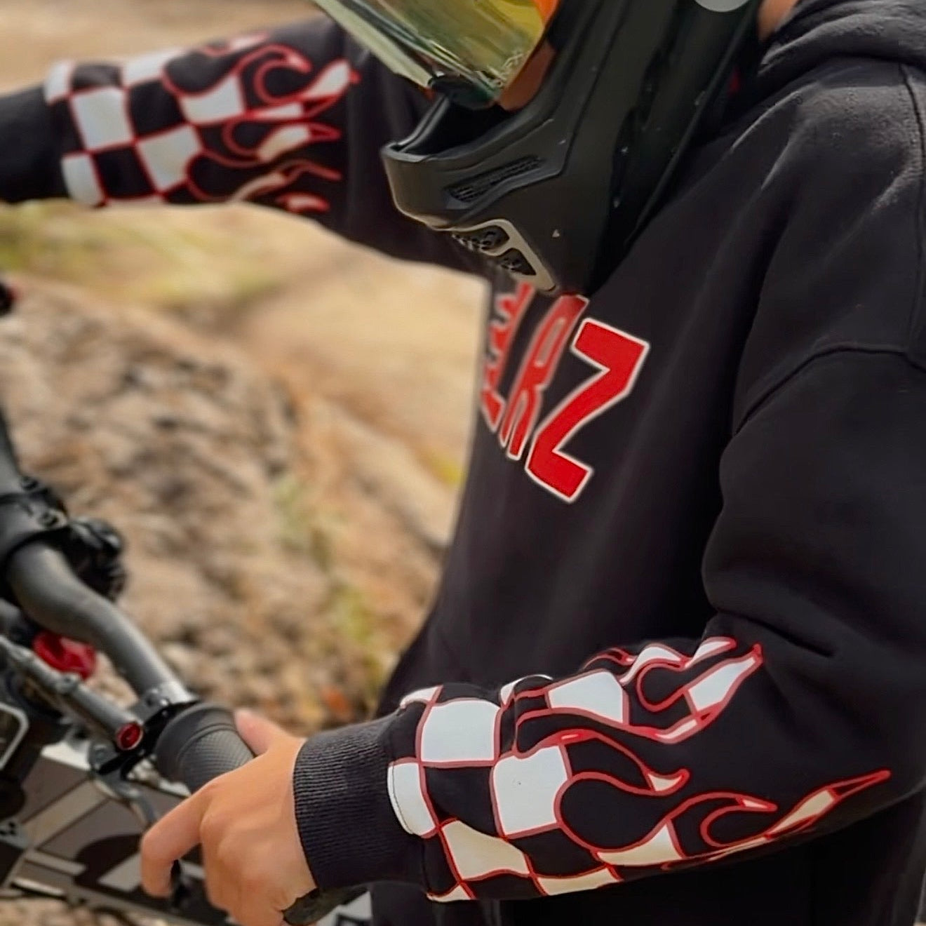 Person wearing a black helmet with orange and white designs, sitting on a dirt bike in an outdoor setting.